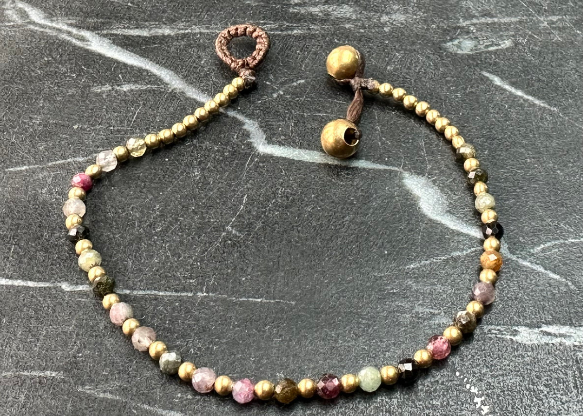 A crystal healing bracelet made of faceted Tourmaline crystals on a cotton cord with brass beads  Edit alt text