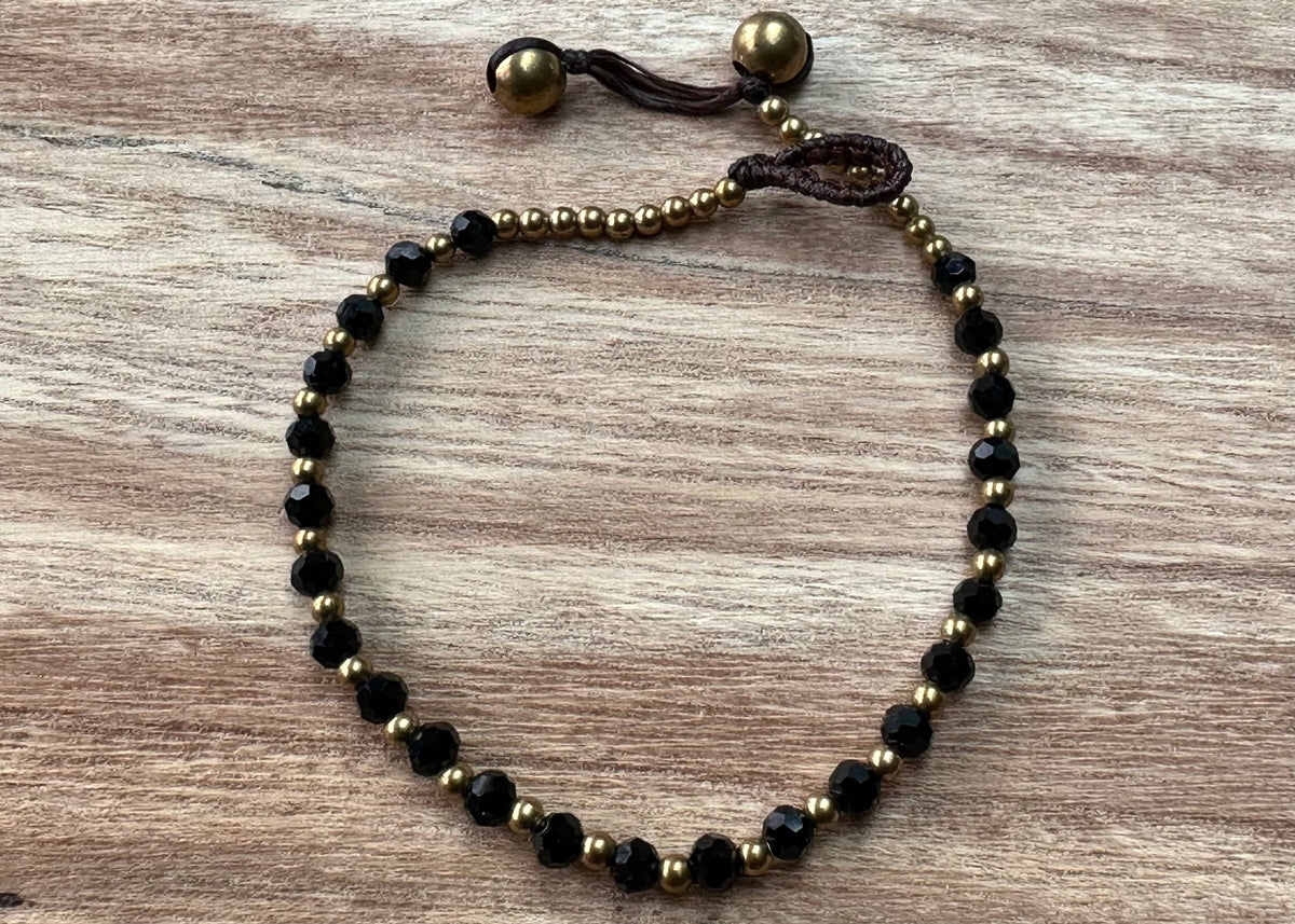 A crystal healing bracelet made of faceted Black Spinel crystals on a cotton cord with brass beads.