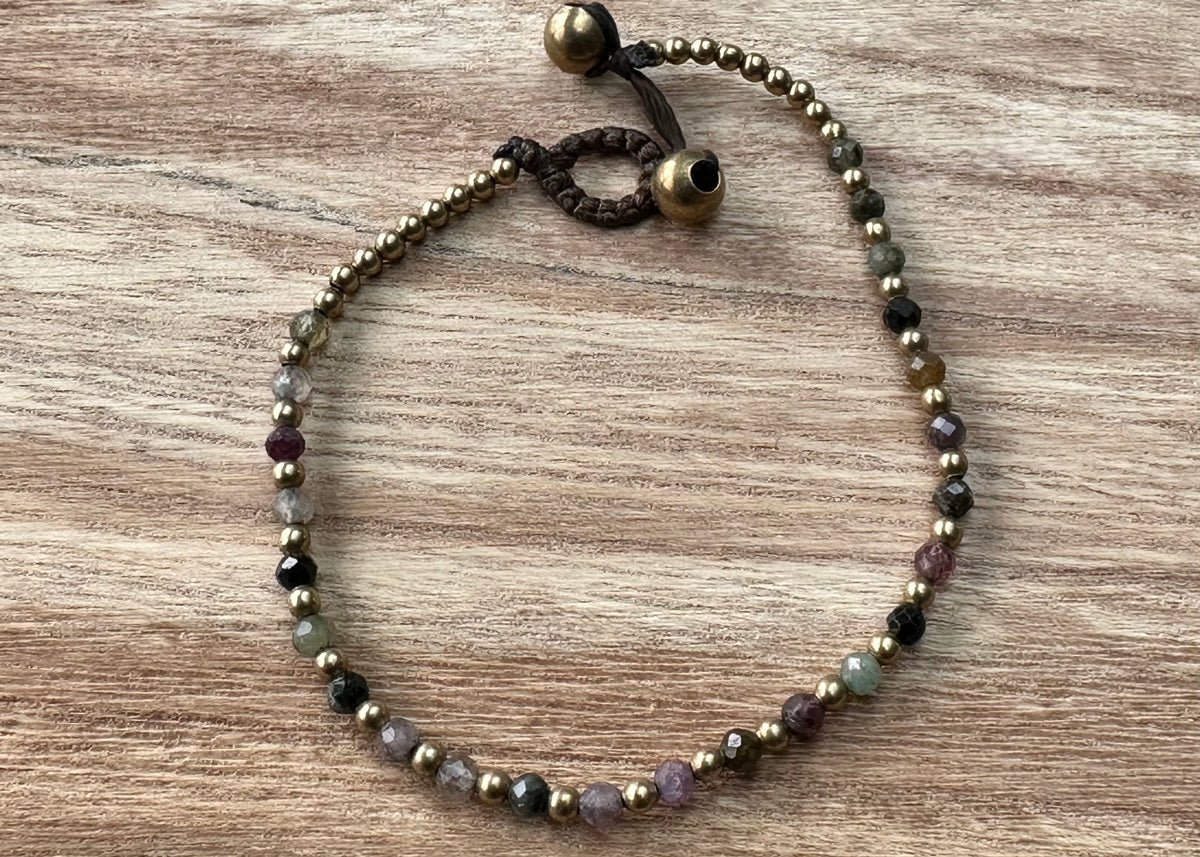 A crystal healing bracelet made of faceted Tourmaline crystals on a cotton cord with brass beads